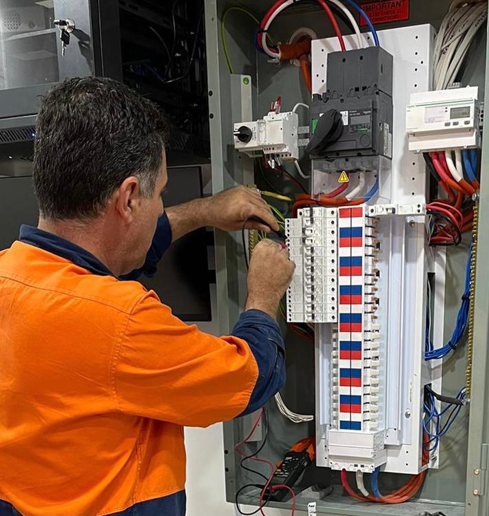 commercial electrician in an orange shirt is focused on working with a control panel, demonstrating concentration and skill.